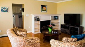 A living room with patterned sofas, a fireplace, a television, and a kitchen visible through an open doorway. - Waterfront Vacation Home-4 bedrooms-2.5bath-Laundry room inside-2 heat pumps (York)