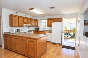 A kitchen with wooden cabinets, a white refrigerator, a microwave, and a stove. - Camp PJs - Coastal Realty Group- Beachfront (Grand Isle)