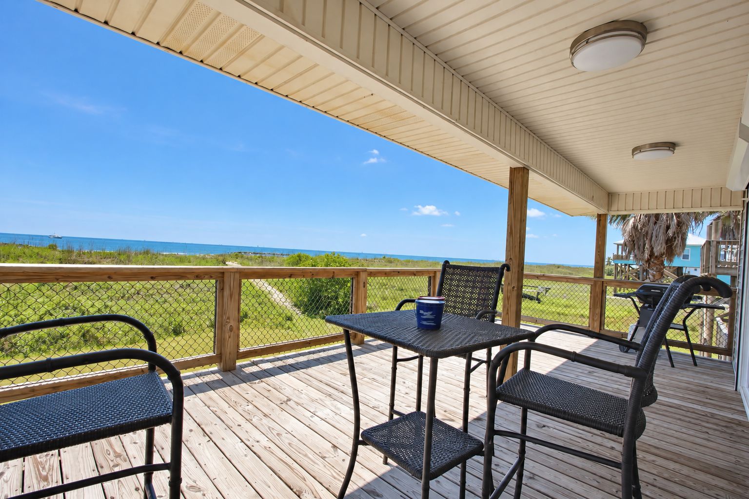 A covered outdoor deck with a view of the ocean, featuring a table and chairs.