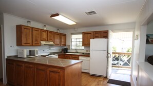 A kitchen with wooden cabinets, a central island, a refrigerator, and a microwave. - Camp PJs - Coastal Realty Group (Grand Isle)