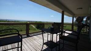 A wooden deck with a table and chairs, overlooking a grassy area and the ocean. - Camp PJs - Coastal Realty Group (Grand Isle)
