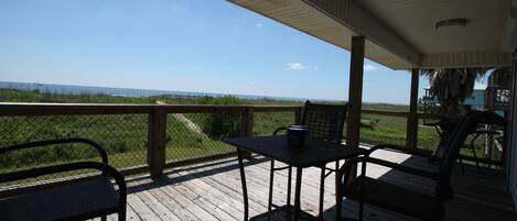 A wooden deck with a table and chairs, overlooking a grassy area and the ocean.