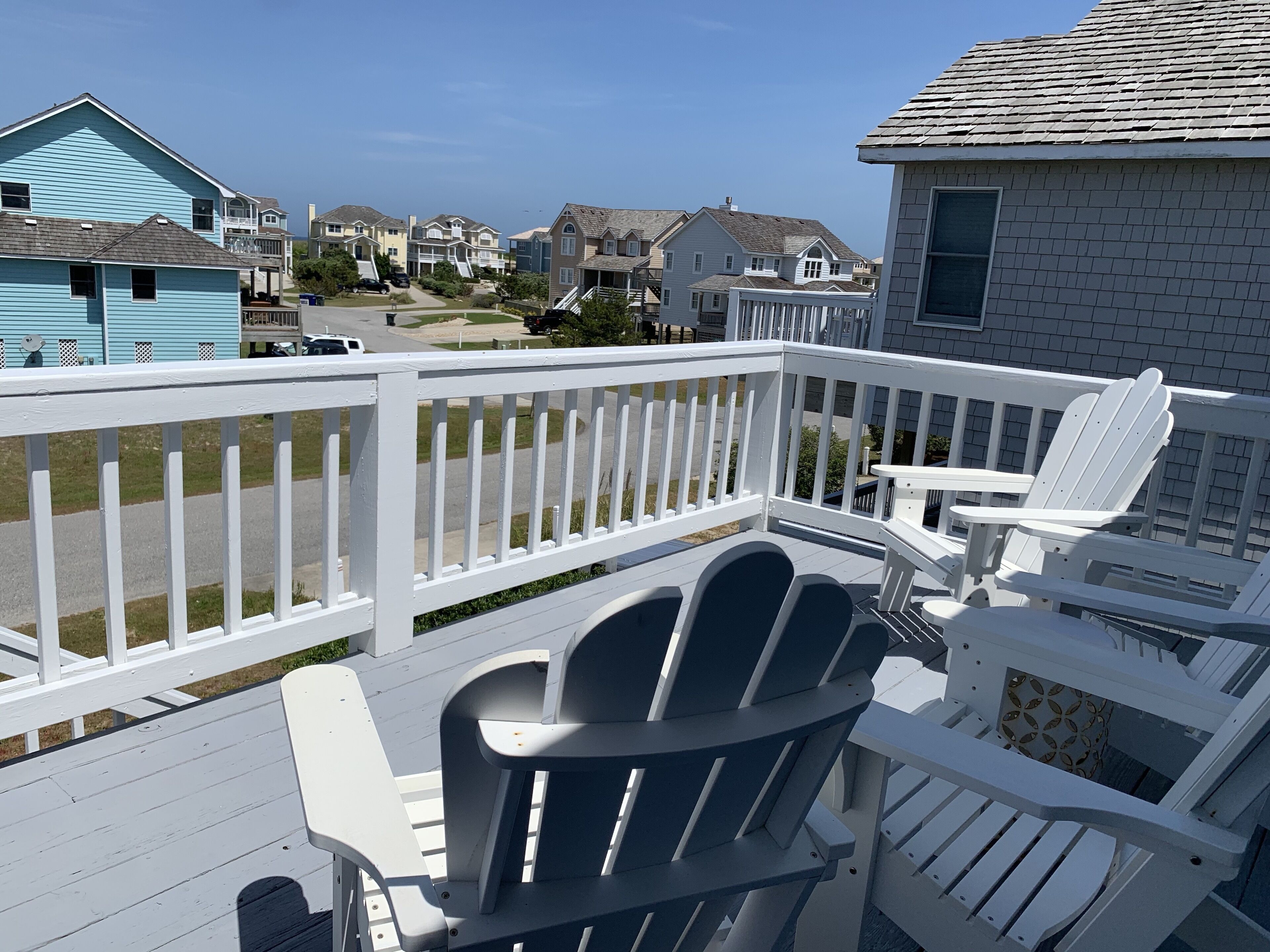 A deck with white railings and Adirondack chairs, overlooking a residential area with houses.