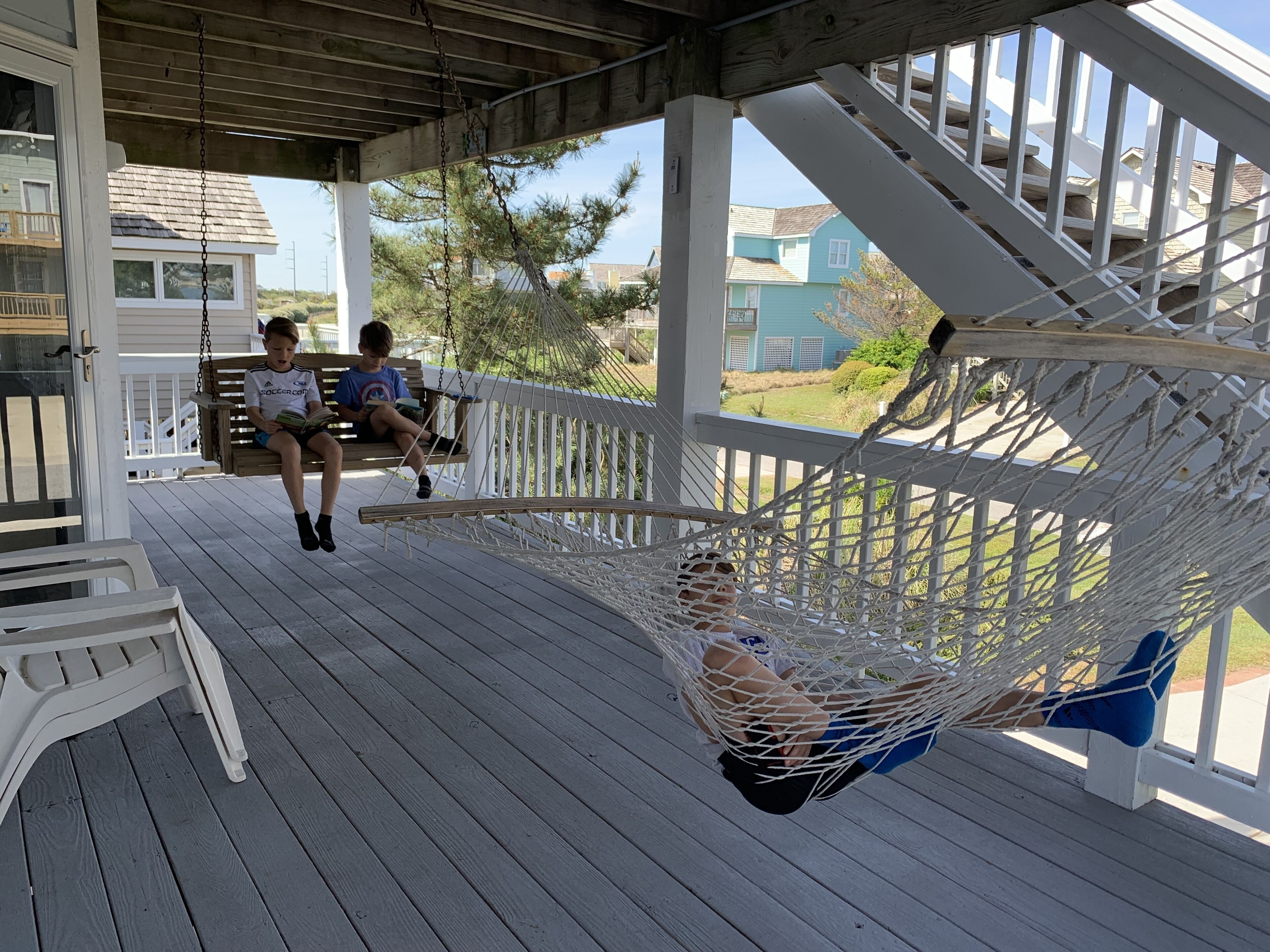 A porch with a wooden deck, a hammock, and two people sitting on a bench.