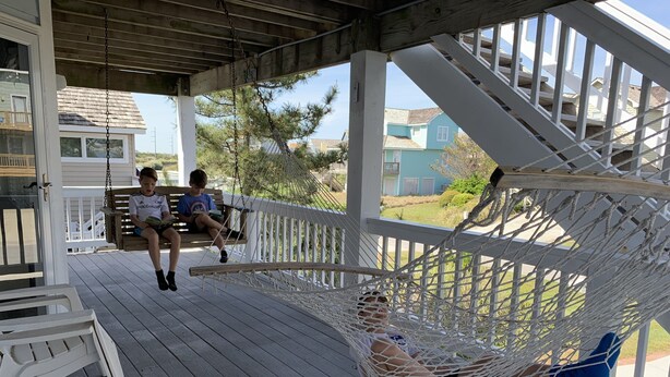 A porch with a wooden deck, a hammock, and two people sitting on a bench.
