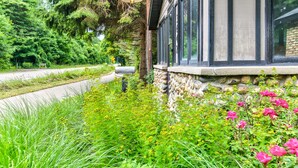 Un edificio de piedra con ventanas amplias, rodeado de abundante vegetación y flores.