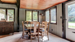 Un comedor con una mesa y sillas de madera, un armario de madera y ventanas amplias con vistas a la vegetación.