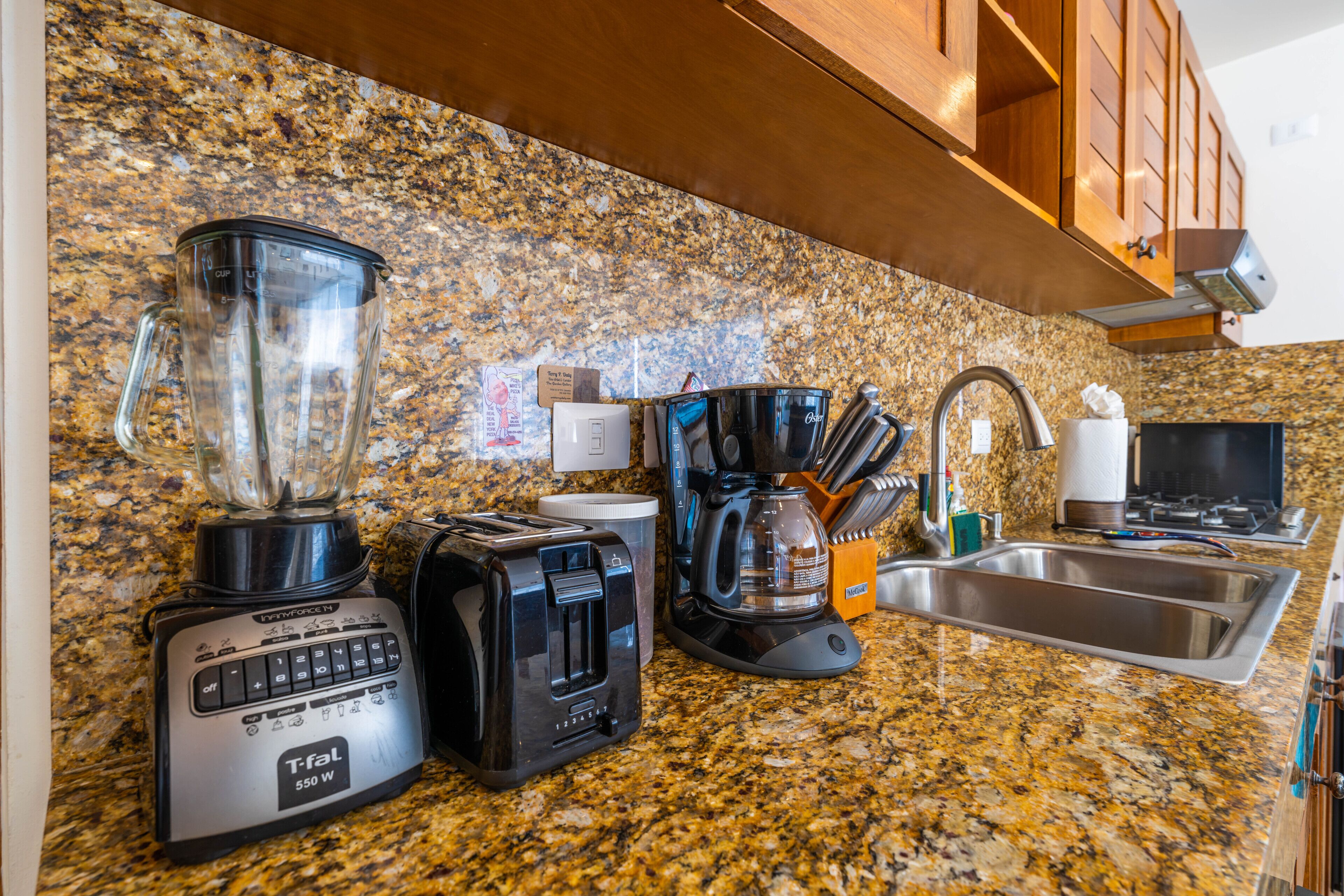 A kitchen with a granite countertop, a blender, a toaster, a coffee maker, and a sink.