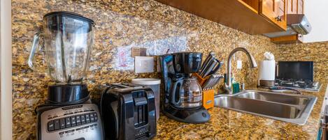 A kitchen with a granite countertop, a blender, a toaster, a coffee maker, and a sink.