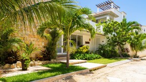 Una casa con fachada de piedra, un porche cubierto y un jardín bien cuidado con palmeras y arbustos.