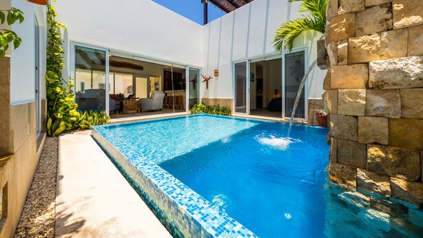 Una piscina con borde de baldosas, rodeada por un muro de piedra y una pérgola.