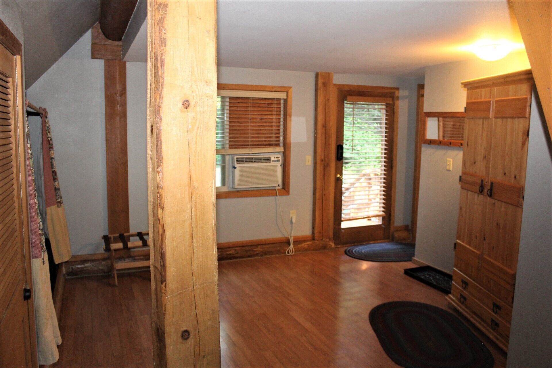 A room with wooden floors, a door with a window, a bench, and a wooden cabinet.