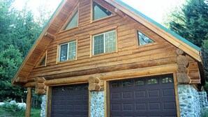A log cabin with a stone foundation, two garage doors, and a triangular roof. - Cozy St. Helen's Cabin is Pet-friendly, Hot tub, AC, WIFI, Seasonal River Access (Randle)