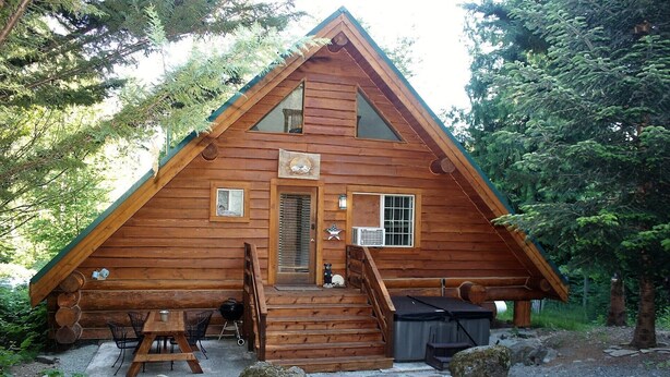 A wooden cabin with a triangular roof, a front porch, and a small deck area. - Cozy St. Helen's Cabin is Pet-friendly, Hot tub, AC, WIFI, Seasonal River Access (Randle)