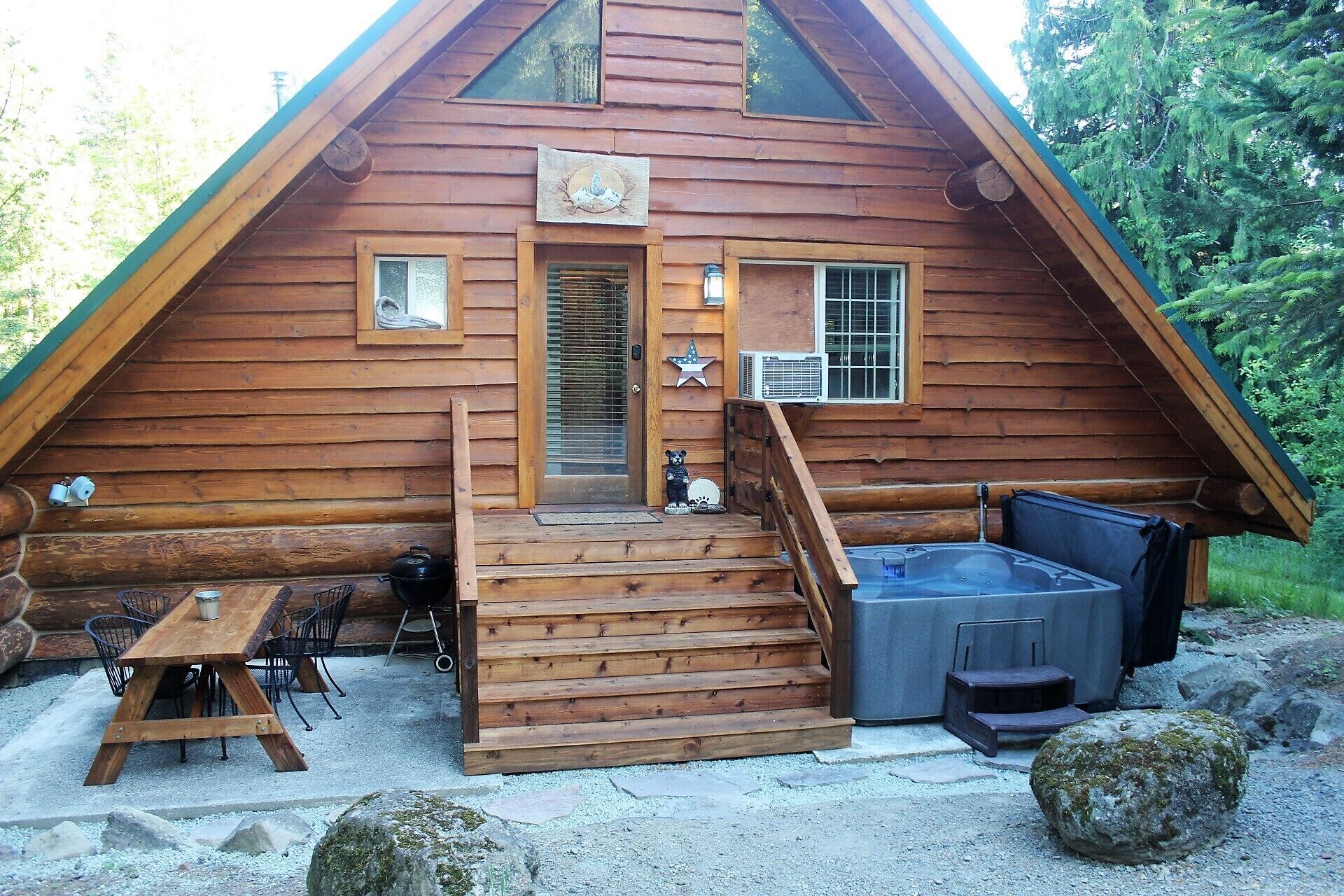 A wooden cabin with a porch, a hot tub, and a table with chairs.