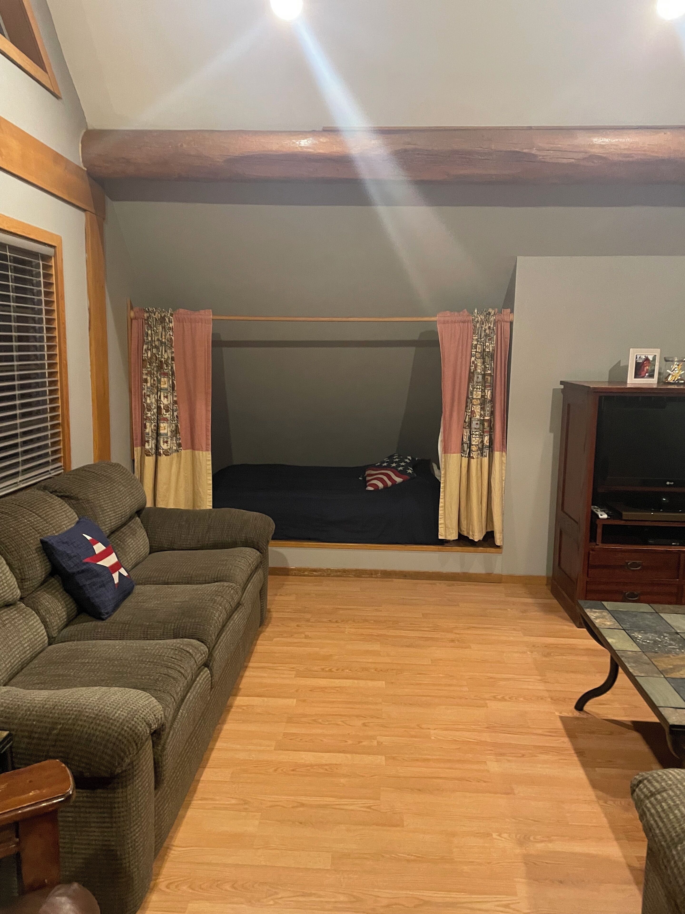 A cozy living room with a sofa, a television, and a window with curtains.