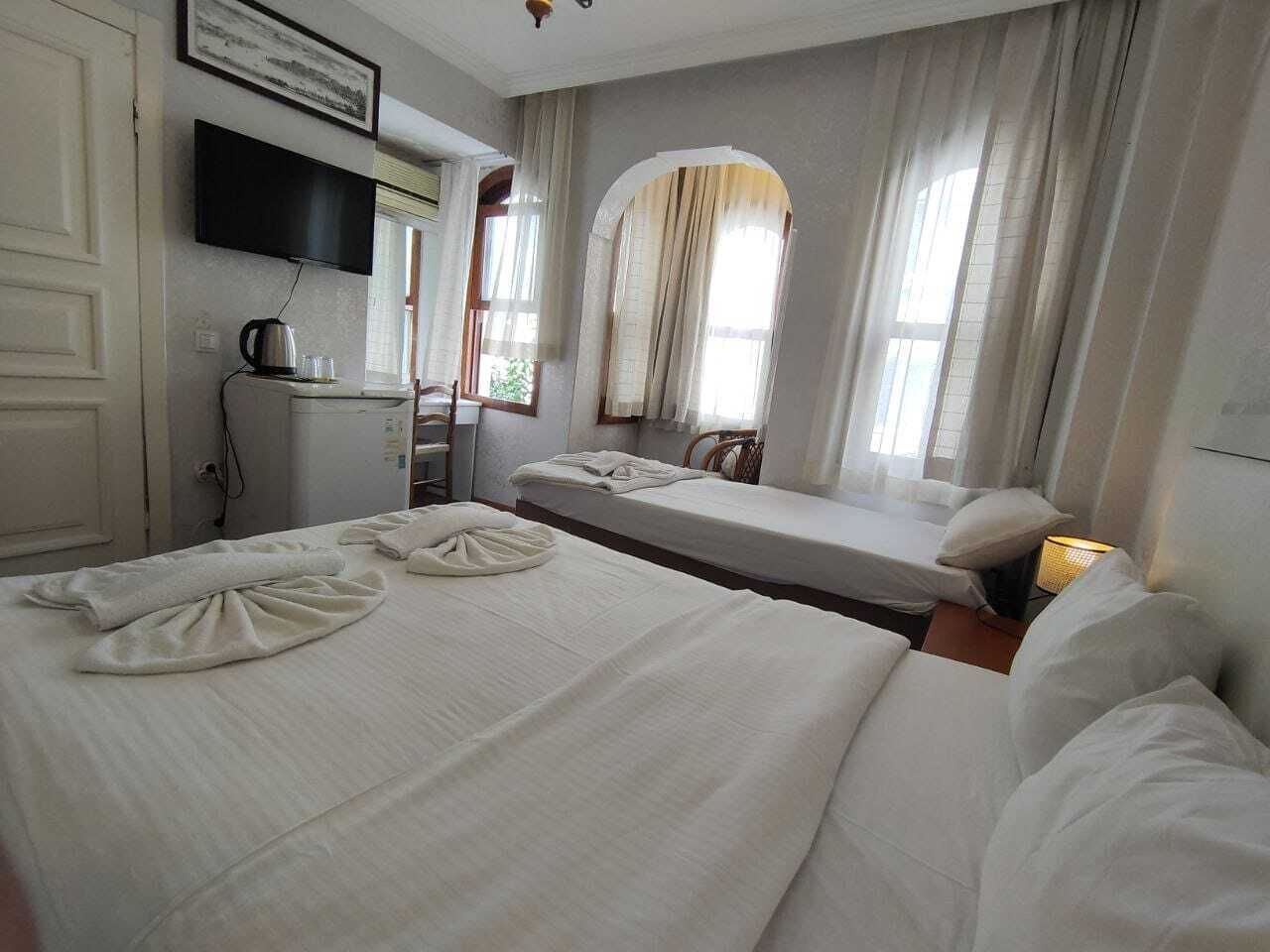A hotel room with two beds, a desk with a kettle, a television, and a window with curtains.