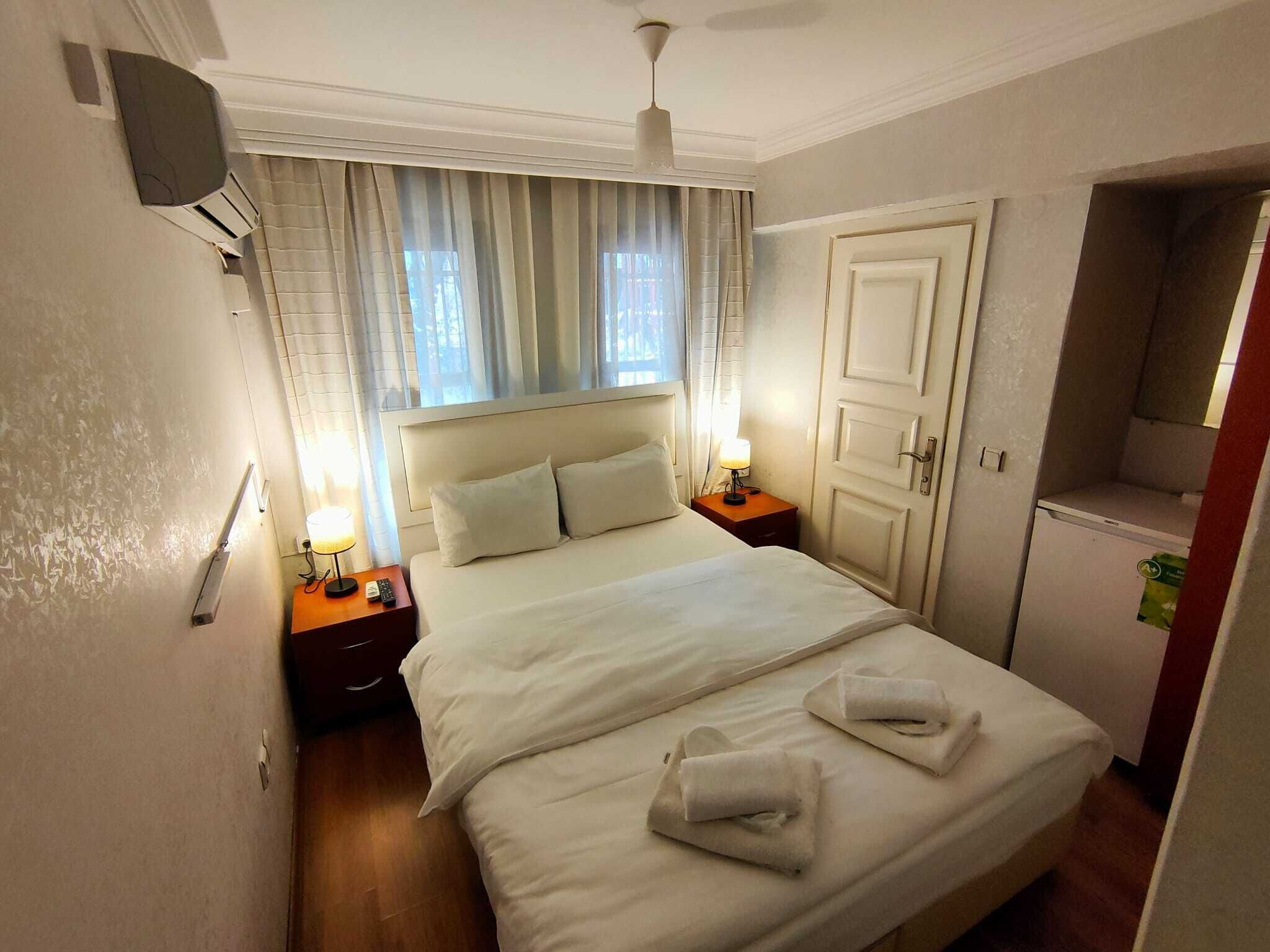 Une chambre d’hôtel avec un lit, deux lampes de chevet, une télévision, une porte et une petite kitchenette.