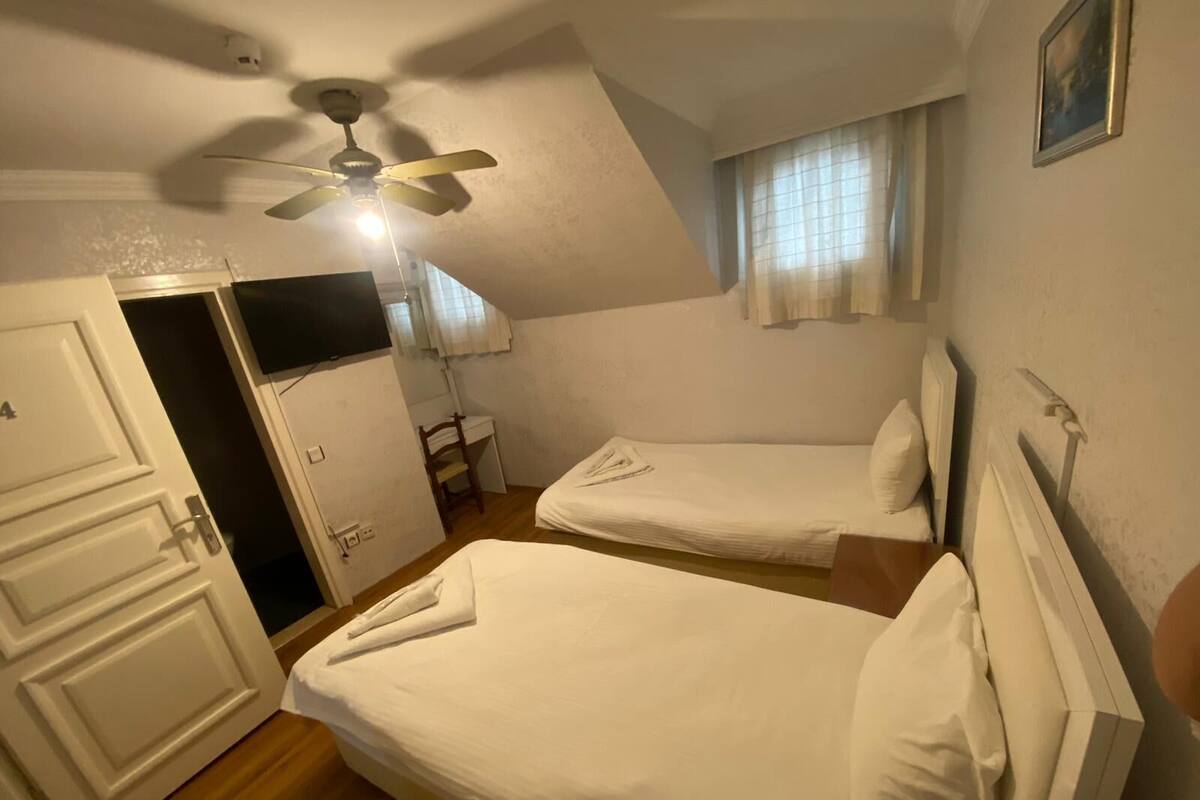 A room with two single beds, a desk, a chair, a ceiling fan, and a door.