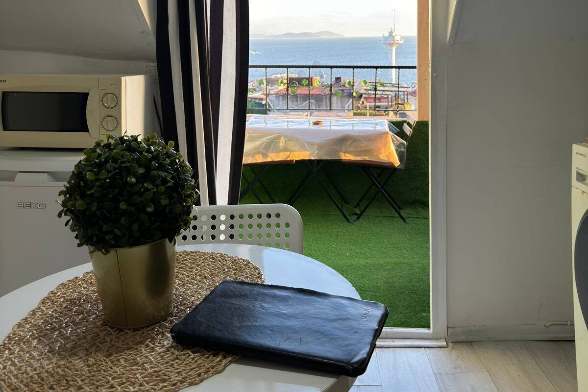 A balcony with a view of the sea, a table with a plant and a black bag, and a white chair.