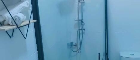 Um banheiro pequeno com box de vidro, vaso sanitário e prateleira com artigos de higiene pessoal.