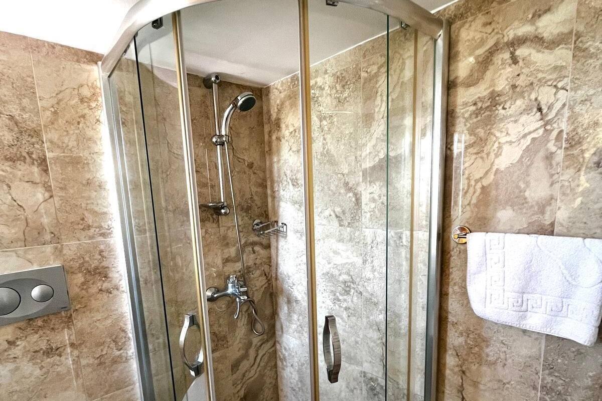 A modern bathroom with a glass-enclosed shower, a toilet, and marble walls.