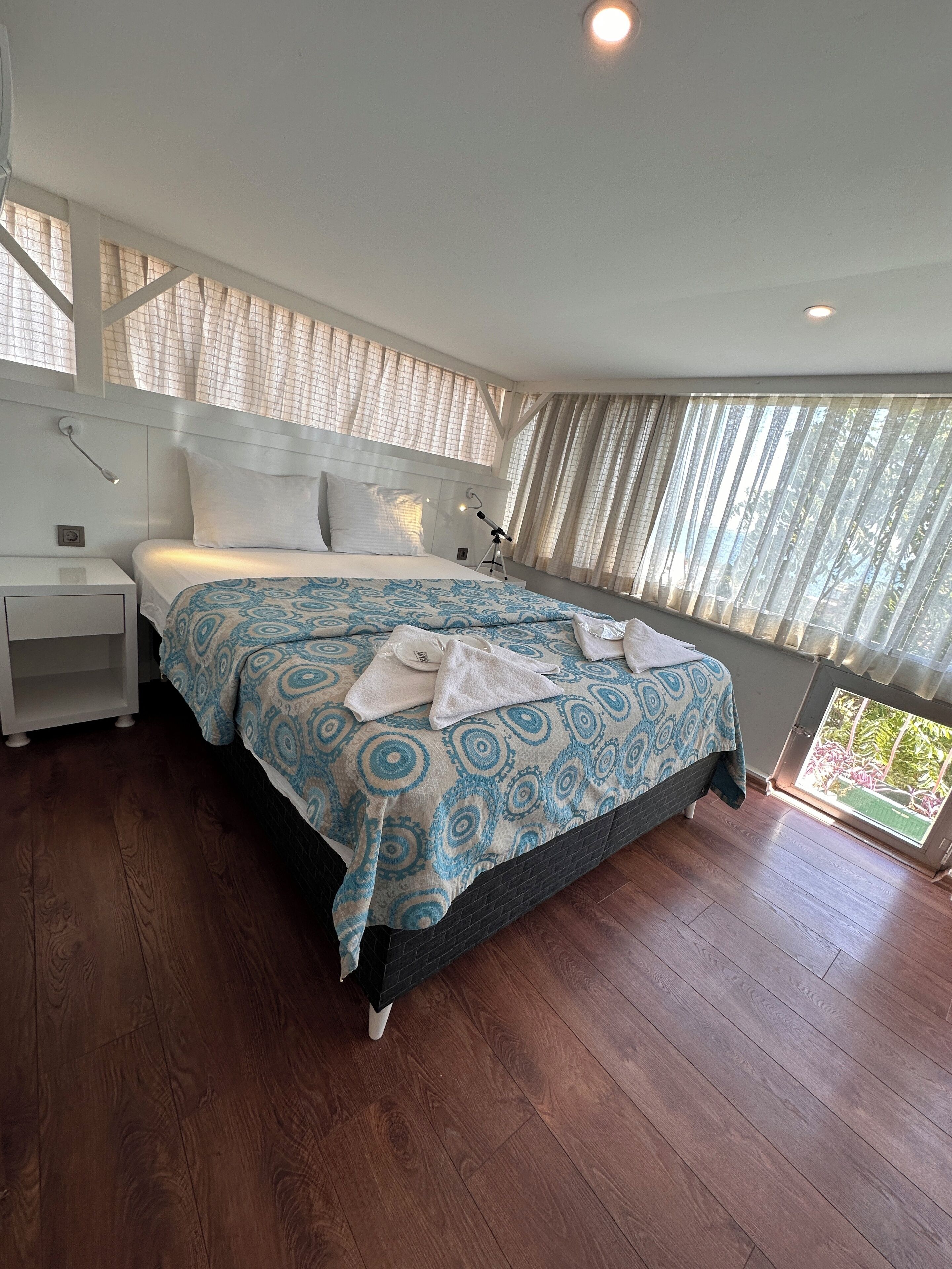 A modern hotel room with a large bed, a nightstand, a desk, and a window with curtains.