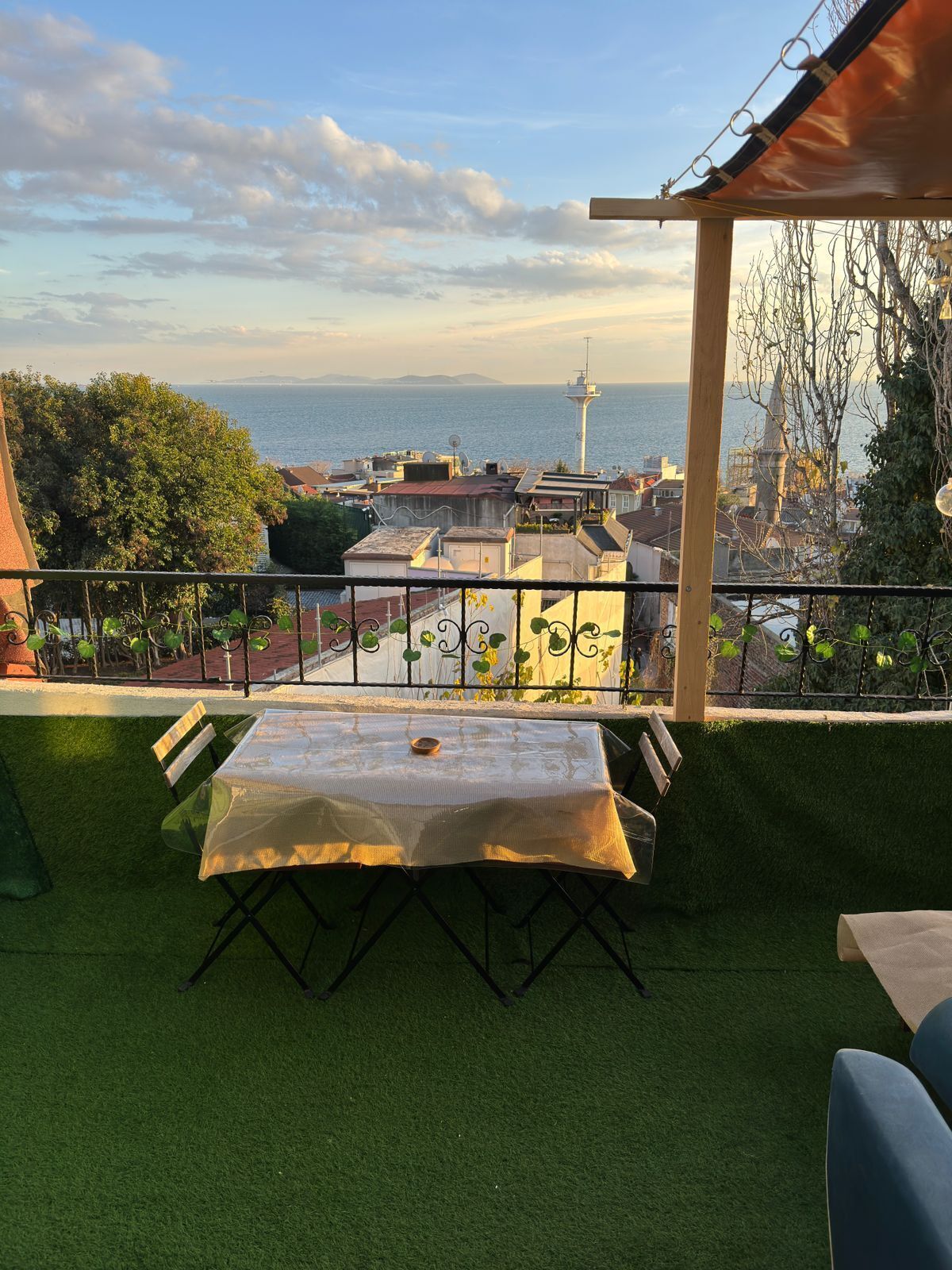 A terrace with a table and chairs, overlooking a cityscape with a tower and the sea.
