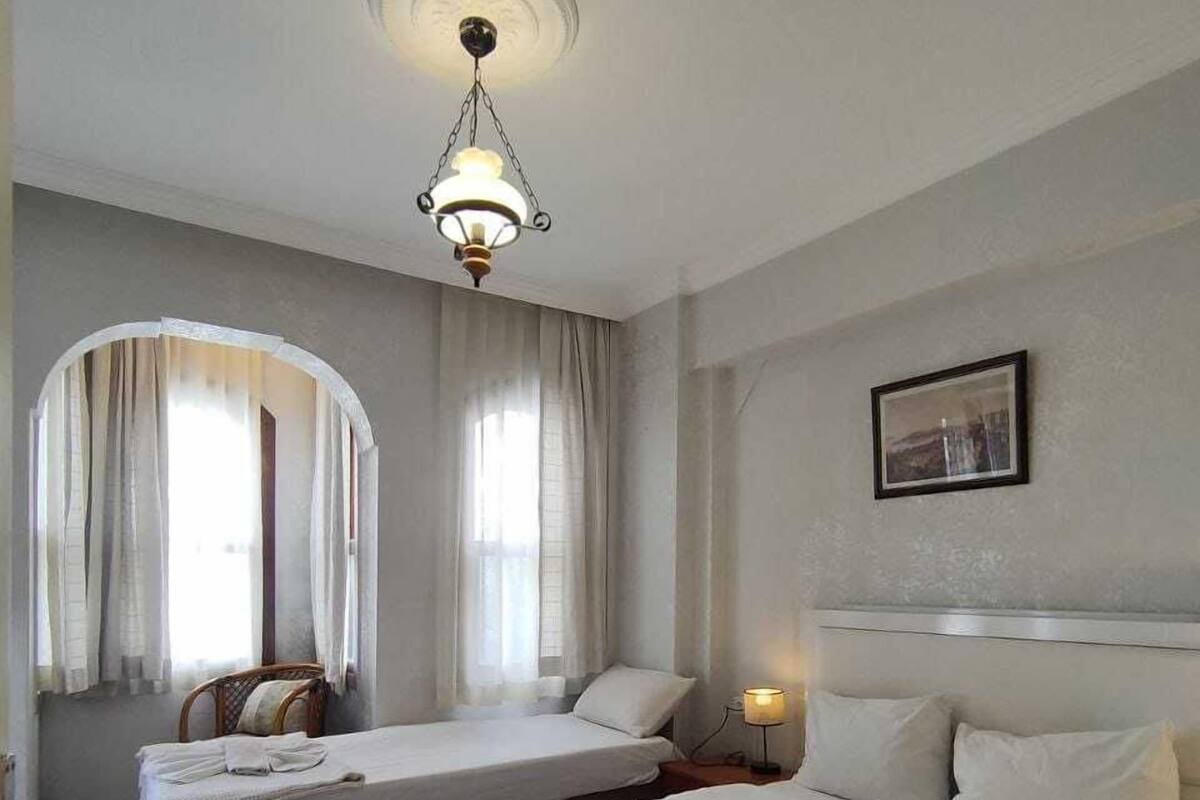A hotel room with two beds, a wooden floor, a chandelier, and a framed picture on the wall.