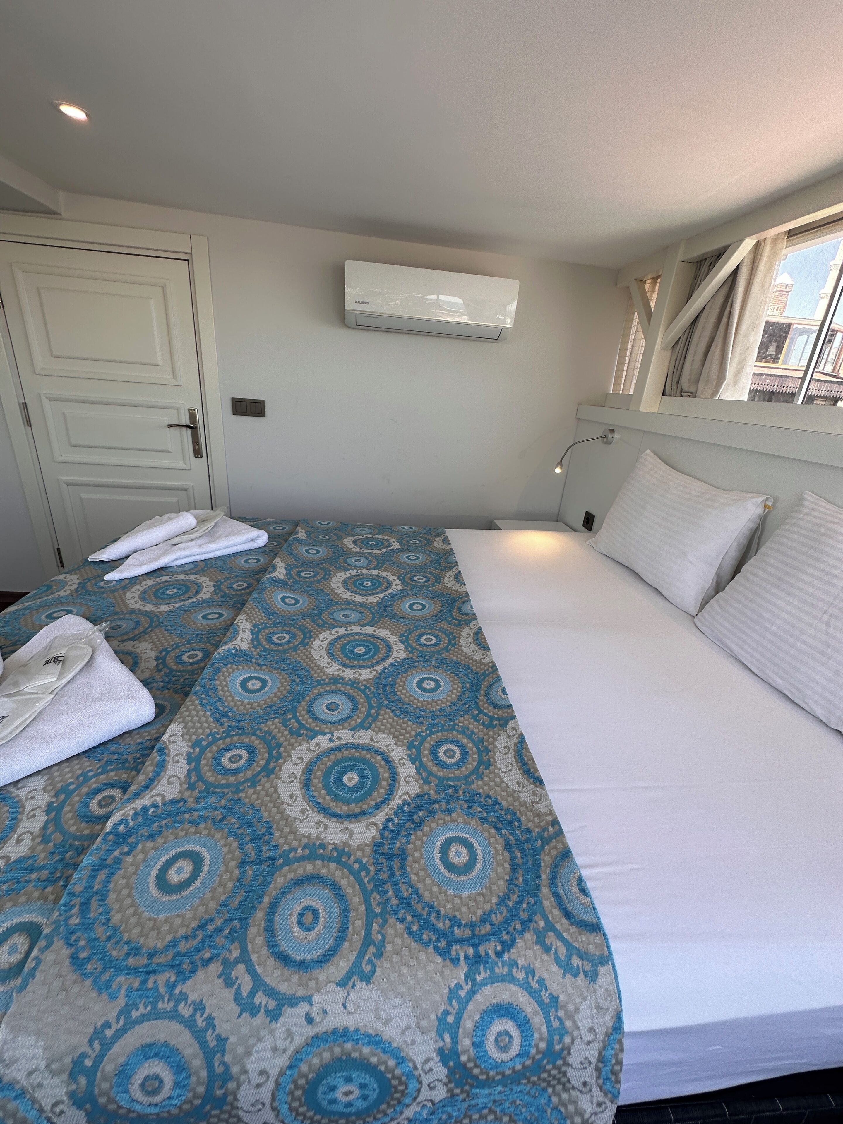 Une chambre d’hôtel avec un lit, une fenêtre, un appareil de climatisation et une porte.
