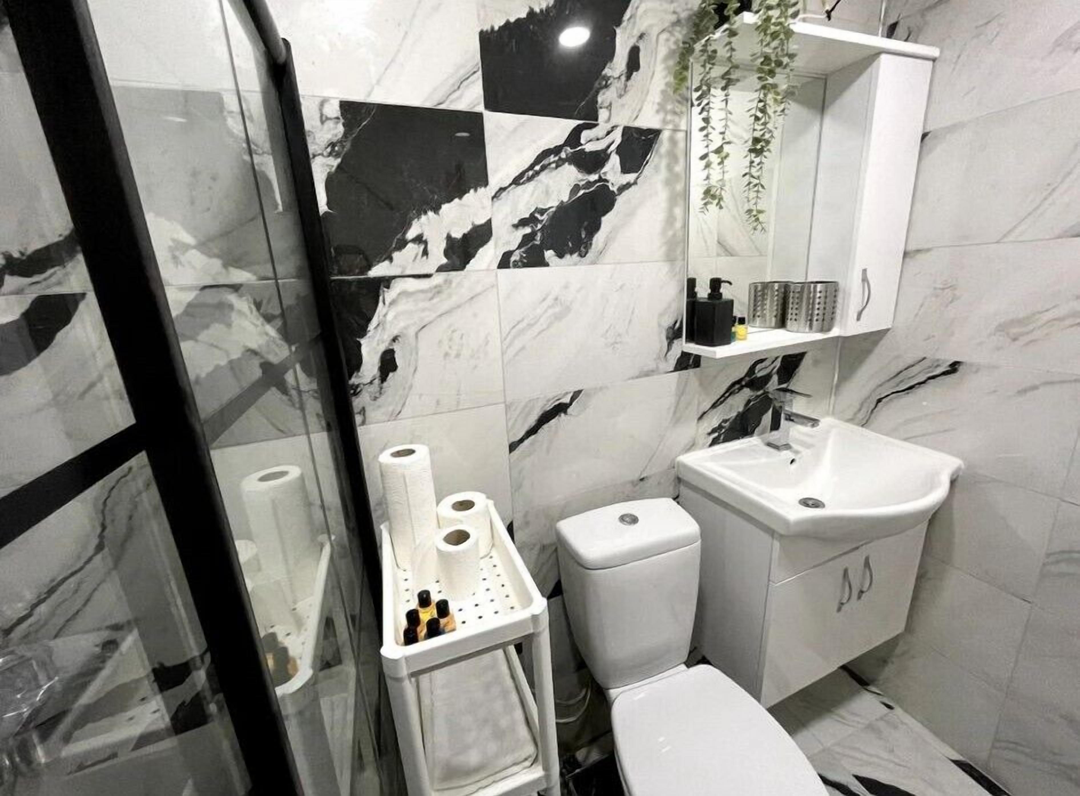A bathroom with a toilet, sink, and a mirror. There are toiletries on the sink and a towel rack.