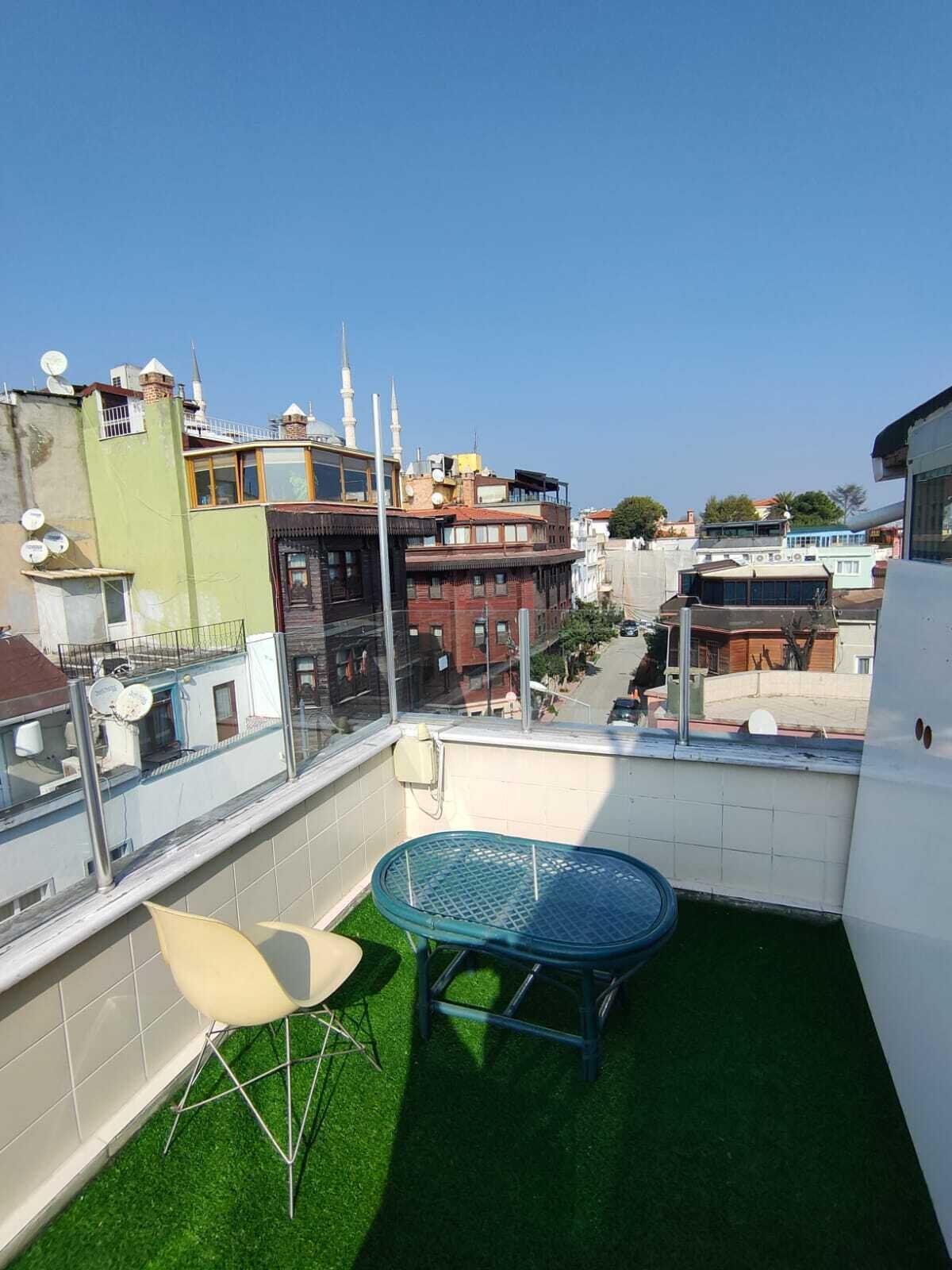 A rooftop terrace with artificial grass, a round table, and two chairs.