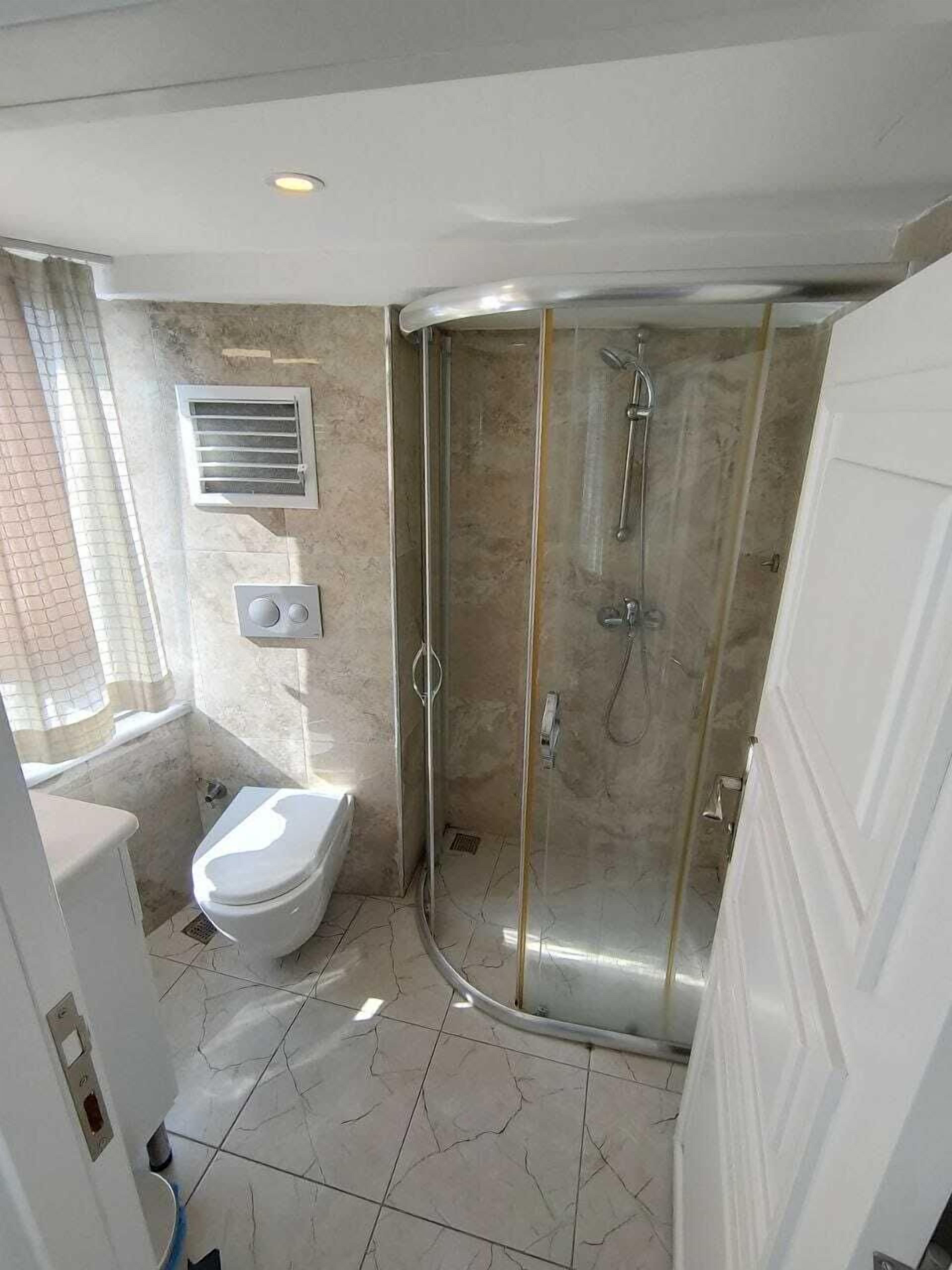 Un baño moderno con cabina de ducha de vidrio, inodoro y ventana con cortina.