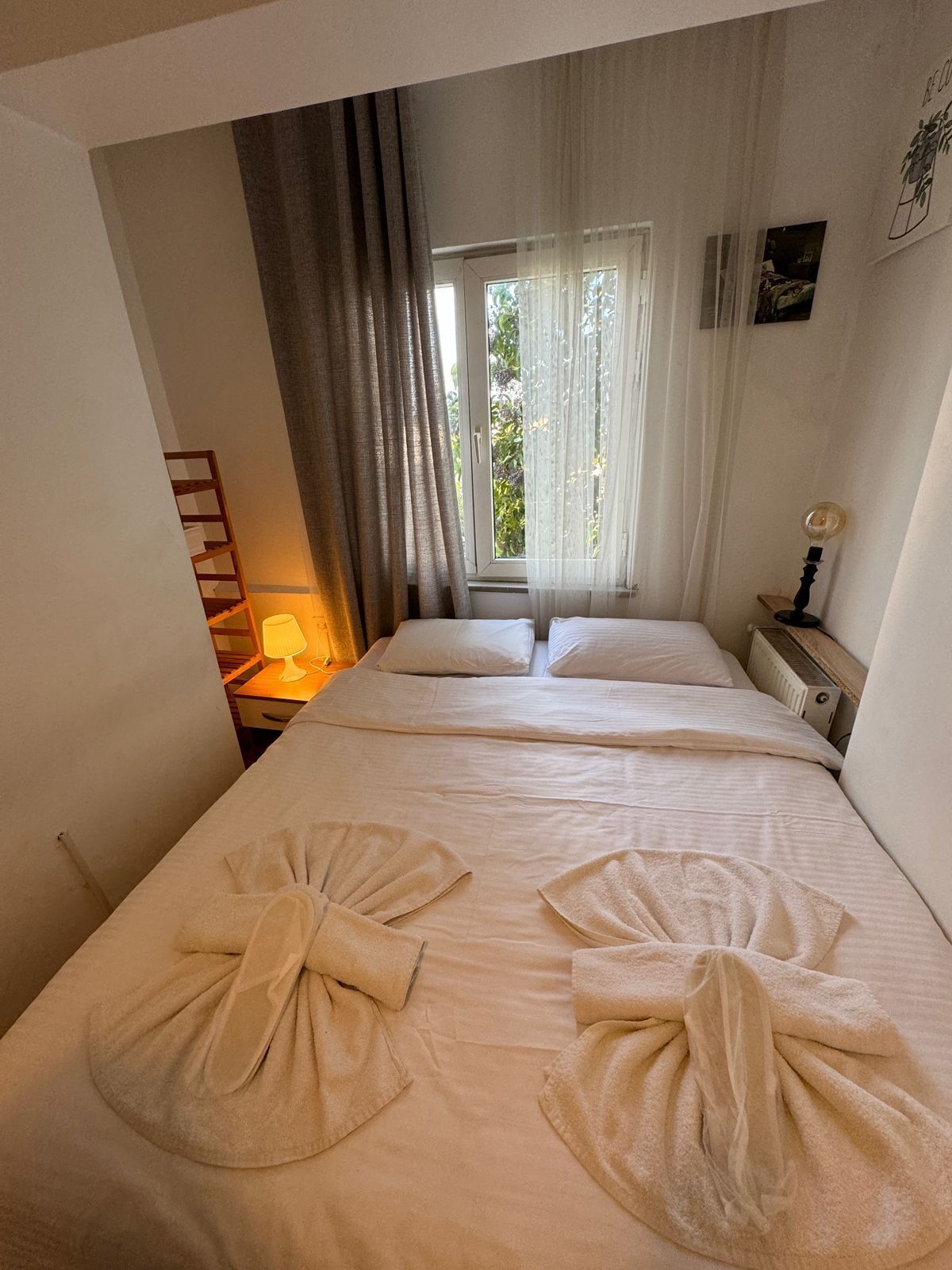 A hotel room with two beds, a window with sheer curtains, a bedside lamp, and a wall-mounted picture.