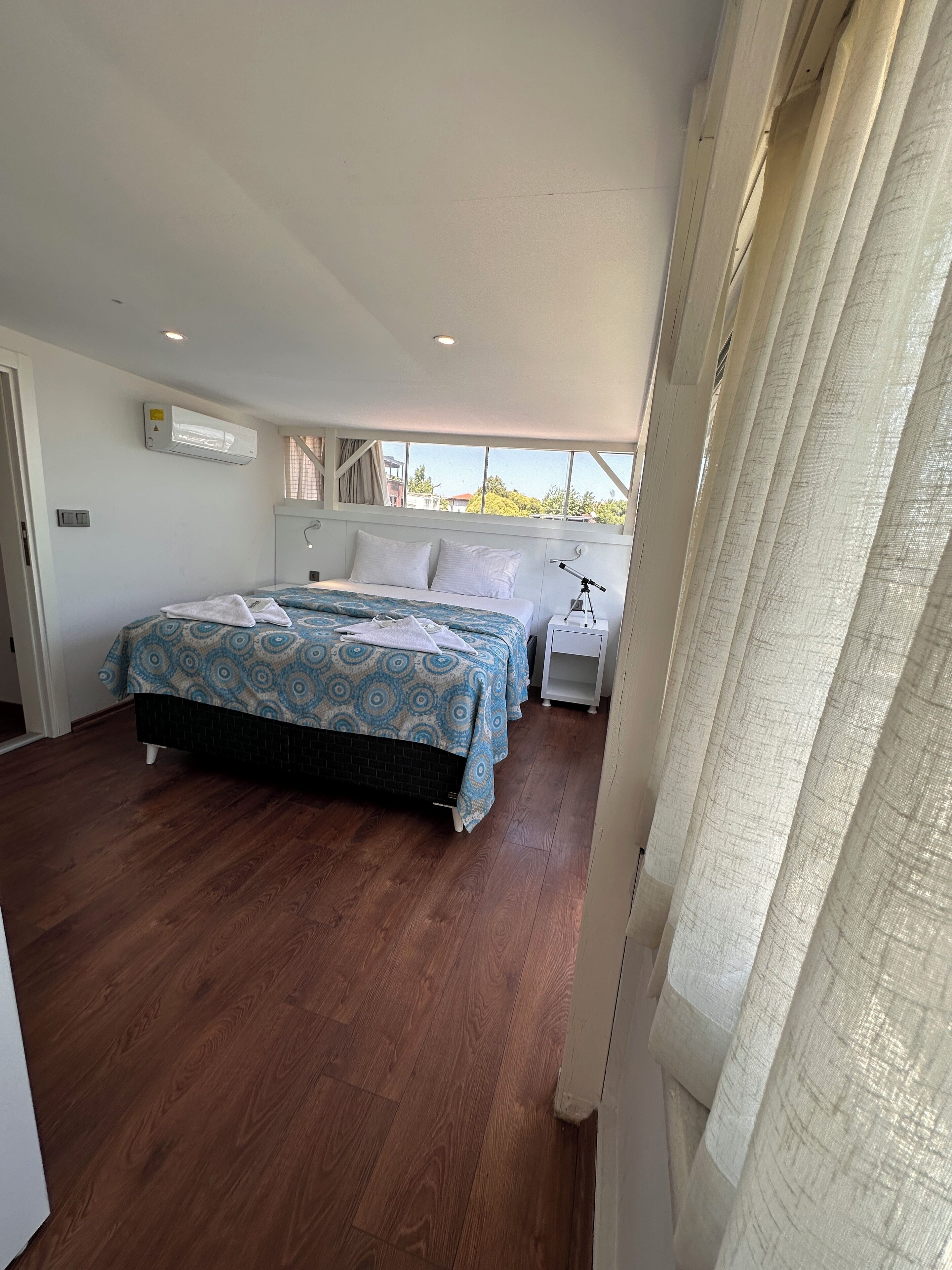 Een slaapkamer met twee bedden, een raam met gordijnen, een witte nachtkastje en een plafondventilator.