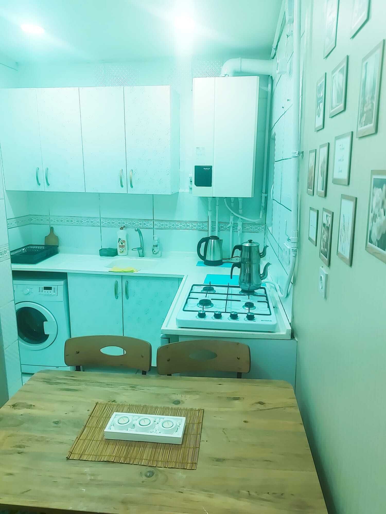 A compact kitchen with white cabinets, a gas stove, a washing machine, and a dining table with a placemat.
