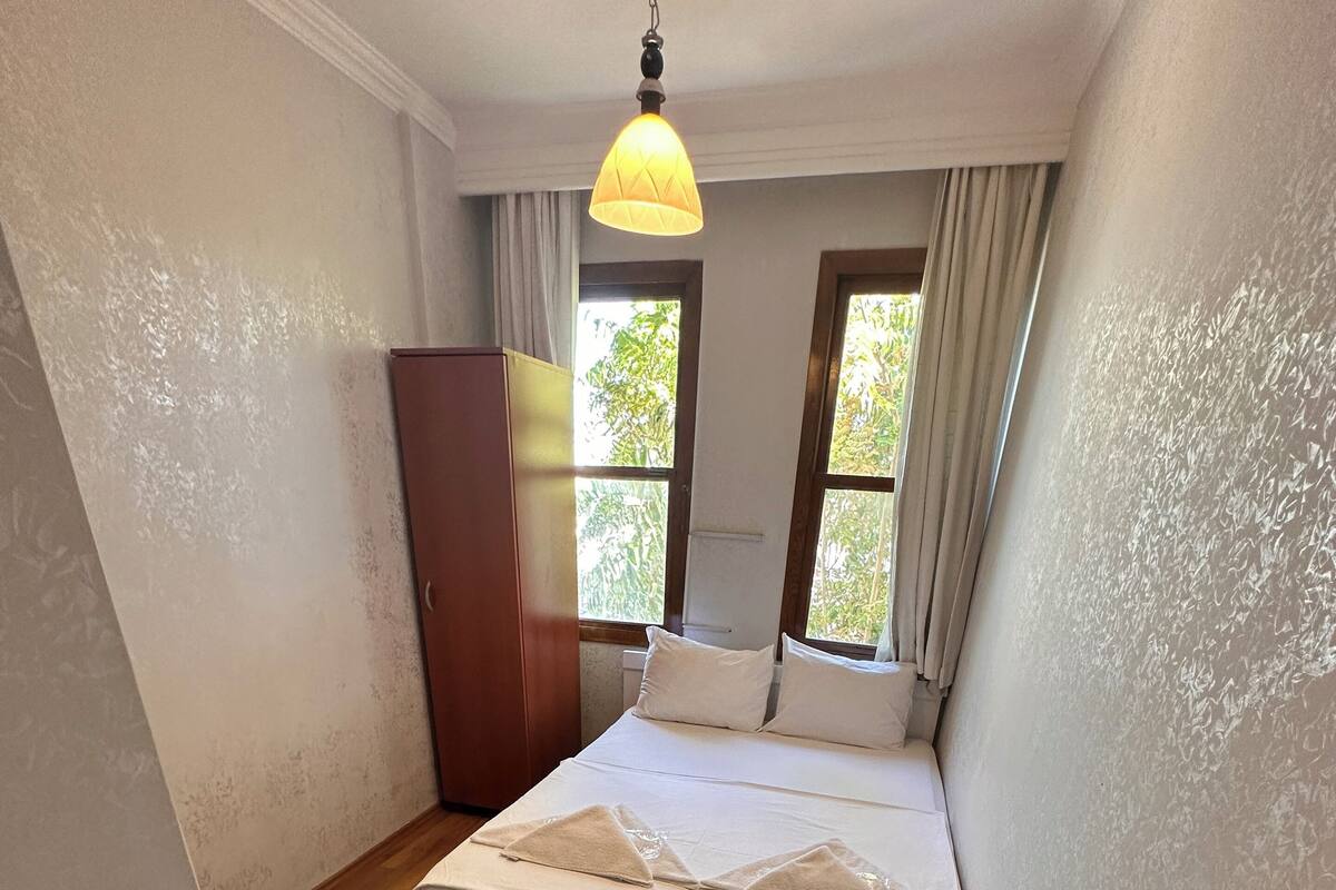 A bedroom with a bed, wooden floor, a wardrobe, and a window with curtains.