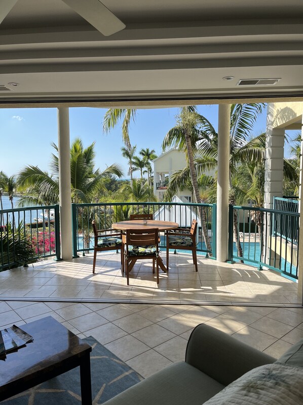 Een balkon met een tafel en stoelen, een zwembad en palmbomen.