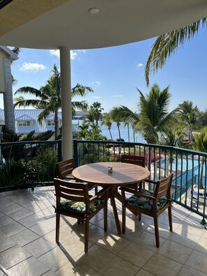 Een ronde houten tafel met stoelen op een balkon, met uitzicht op een zwembad en palmbomen.