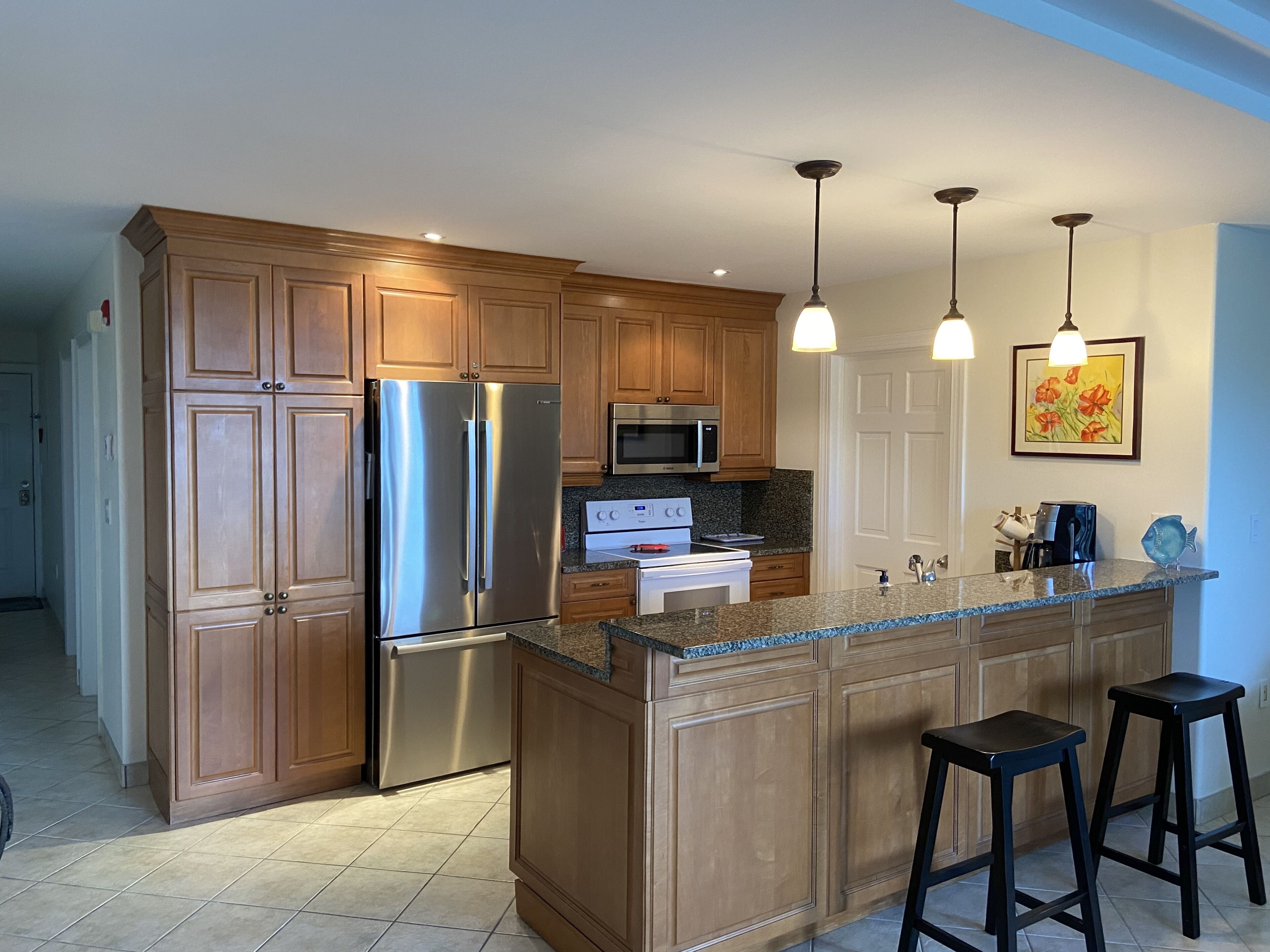 A kitchen with wooden cabinets, stainless steel appliances, granite countertops, and two bar stools.