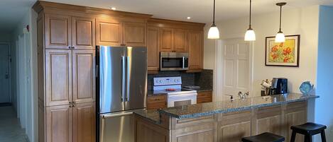 A kitchen with wooden cabinets, stainless steel appliances, granite countertops, and two bar stools.