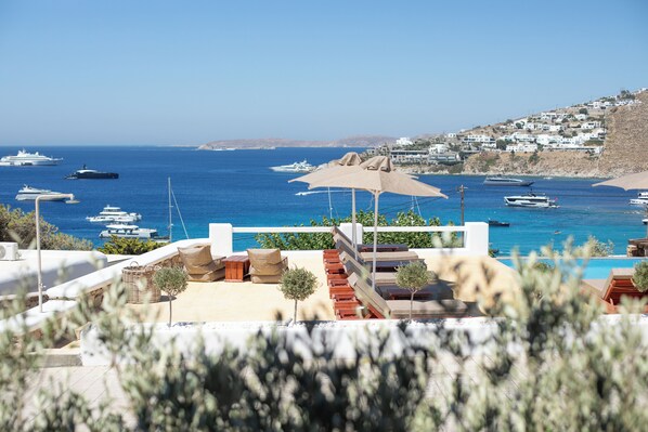 A coastal view with a pool area, lounge chairs, and umbrellas. - Seethrough Mykonos - Adults Only (Mykonos)