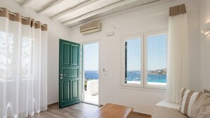 A room with a wooden bench, a sofa, a green door, and a view of the sea. - Seethrough Mykonos - Adults Only (Mykonos)