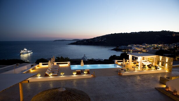 A rooftop pool area with a view of the sea, a boat, and a hillside town. - Seethrough Mykonos - Adults Only (Mykonos)