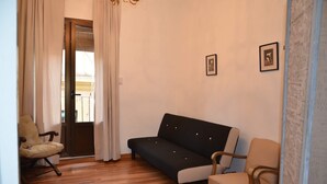 A living room with a sofa, two chairs, a wooden floor, and a door with curtains. - Apartment Cos del Bou (Tarragona)