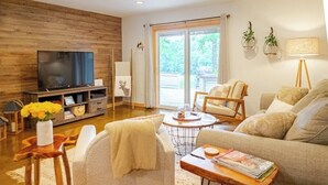 A modern living room with a flat-screen TV, comfortable seating, a coffee table, and a large window with a view of greenery. - Alpine in the Ozarks~ right off back 40 trails (Bella Vista)