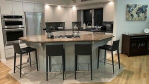 Une cuisine moderne dotée d’un îlot central, d’appareils électroménagers en acier inoxydable et de tabourets de bar.
