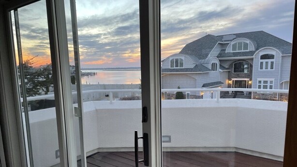 Un coin d’une pièce avec une terrasse en bois et une vue sur une grande maison située de l’autre côté d’une étendue d’eau.
