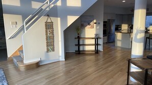 Un vaste espace de vie doté d’un plancher en bois, d’un escalier et d’une cuisine à l’arrière-plan.