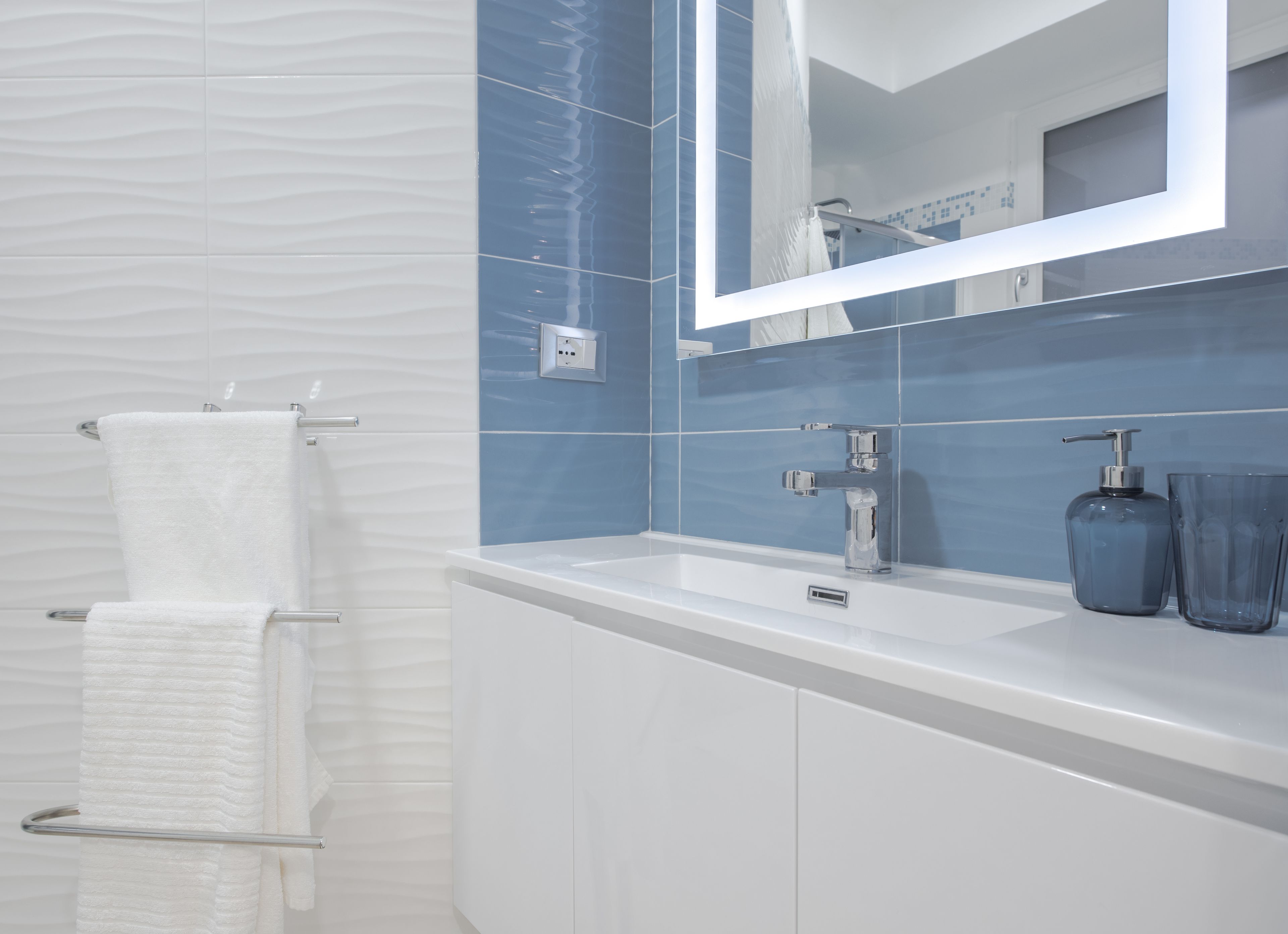 A modern bathroom with a white vanity, a large mirror, and a blue tiled wall.